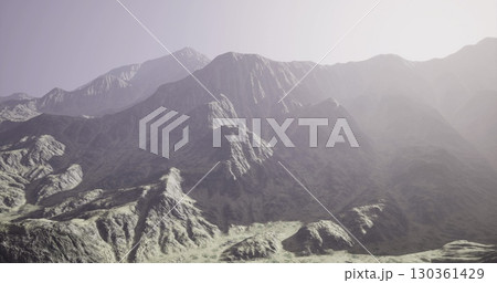 Rugged mountain terrain stretches majestically under a gentle light, highlighting the intricate details of the rocky peaks and valleys during a tranquil evening. 130361429