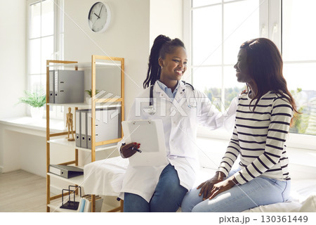 Doctor holding report file with appointment and listening her woman patient in clinic. 130361449