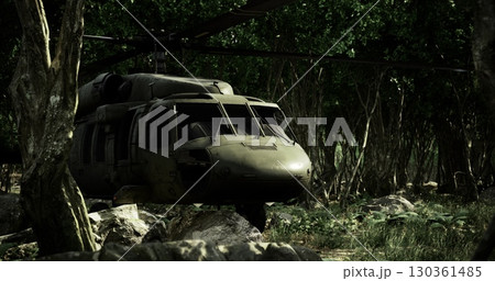 A military helicopter stands still among lush green trees and rocks. The area is quiet, marked by an overcast sky that casts a muted light on the surroundings. A military helicopter stands still among lush green trees and rocks. The area is quiet, marked by an overcast sky that casts a muted light on the surroundings. 130361485