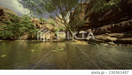 Clear waters reflect rock formations in this tranquil oasis surrounded by lush greenery. The sunlight illuminates the stunning natural features under a bright sky. 130361487