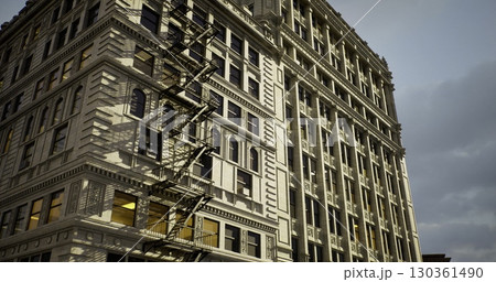A vintage building showcases intricate architectural details under a twilight sky. The fire escape adds character to the structure, capturing the essence of urban design. A vintage building showcases intricate architectural details under a twilight sky. The fire escape adds character to the structure, capturing the essence of urban design. 130361490