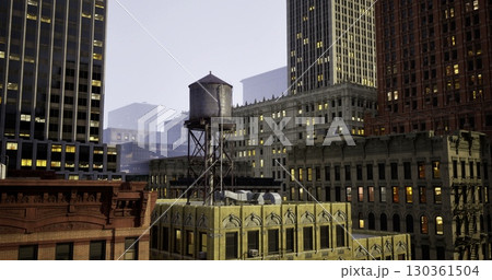 A historic water tower is prominently placed atop a yellow building, surrounded by skyscrapers under a dusky sky, showcasing the blend of architecture and urban life after sunset. 130361504