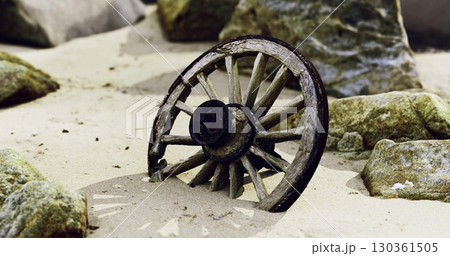 A wooden wagon wheel rests among sandy soil and scattered rocks. Its weathered surface and strategic positioning suggest a long lost history in this natural setting. 130361505