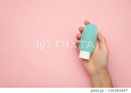 Hand holding blank blue plastic tube on pink background. Cosmetic beauty product branding mockup. Hand holding blank blue plastic tube on pink background. Cosmetic beauty product branding mockup. 130361647