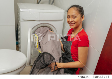 A Woman Happily Engaged in Doing Laundry at Home Using Her Washing Machine A Woman Happily Engaged in Doing Laundry at Home Using Her Washing Machine 130361751