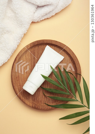 White cosmetic tube on wooden plate with green leaves on beige background. 130361964