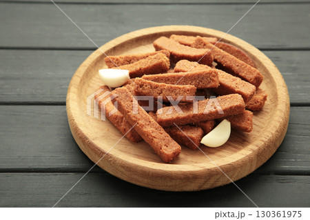 Tasty rye croutons on wooden plate on black background. Tasty rye croutons on wooden plate on black background. 130361975