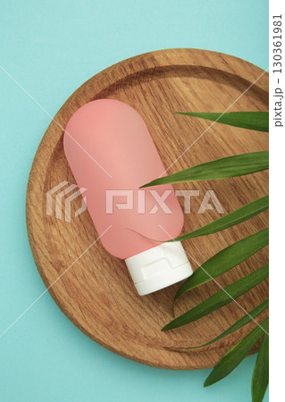 Pink cosmetic tube for travel on wooden plate with green leaves on blue background. 130361981