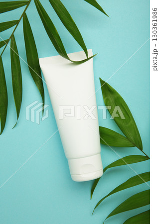 White cosmetic tube with green leaves on blue background. 130361986