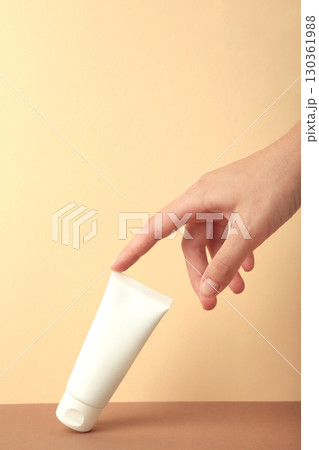 Hand holding blank white plastic tube on beige background. Vertical photo Hand holding blank white plastic tube on beige background. Vertical photo 130361988