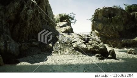 Rocky coastline with textured stones and scattered plant life near tranquil water under a clear blue sky during daylight. Natural setting evokes peace and solitude. 130362294