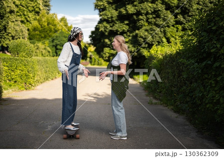 Friends enjoying a sunny day while practicing skateboarding tricks outdoors 130362309