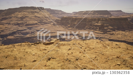 Vast expanse of rugged canyon formations under soft golden light, revealing intricate textures and shadows. A serene atmosphere envelops the breathtaking landscape during sunset. Vast expanse of rugged canyon formations under soft golden light, revealing intricate textures and shadows. A serene atmosphere envelops the breathtaking landscape during sunset. 130362358