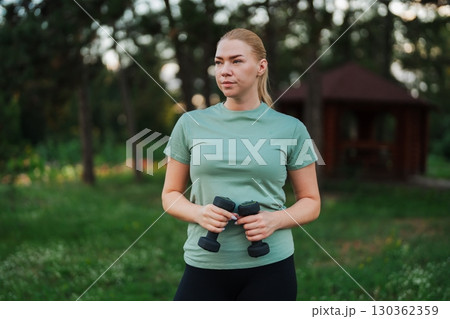 Strong woman with weights exercises in a serene outdoor setting Strong woman with weights exercises in a serene outdoor setting 130362359