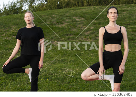 Two women practicing yoga poses on a sunny day in a green park 130362405