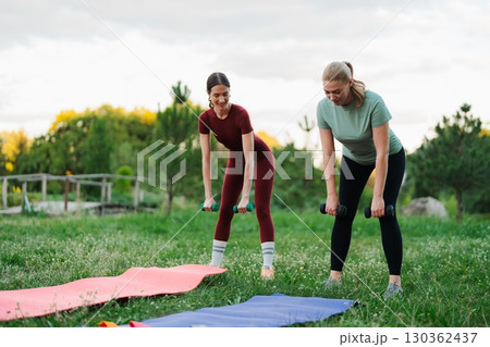 Two friends exercising outdoors with weights on yoga mats in nature 130362437
