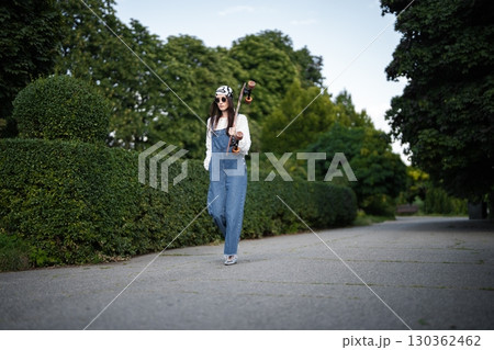 Confident skateboarder strolls through a lush green park on a sunny day 130362462