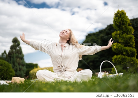 Joyful woman enjoying a sunny picnic in a lush green park under clouds 130362553