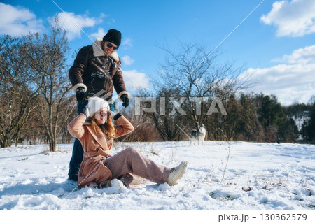 Couple enjoying winter fun in snowy landscape with a dog nearby Couple enjoying winter fun in snowy landscape with a dog nearby 130362579