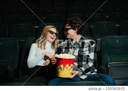 Couple enjoys a movie date while sharing popcorn in a theater Couple enjoys a movie date while sharing popcorn in a theater 130362633