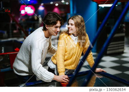 Couple enjoying a friendly game of air hockey in an arcade setting 130362634