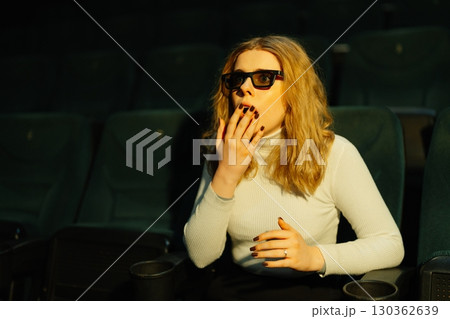 Woman enjoying a suspenseful movie in a theater during evening show Woman enjoying a suspenseful movie in a theater during evening show 130362639