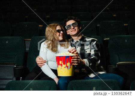 Young couple enjoying a movie date night with popcorn in a theater Young couple enjoying a movie date night with popcorn in a theater 130362647