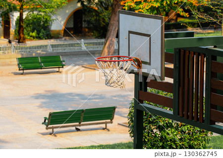 Natural park walking area with basketball hoop and green benches in summertime 130362745