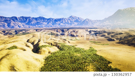 Expansive desert terrain unfolds under a bright blue sky, with verdant patches of vegetation contrasting against rugged mountains in the distance, creating a serene and captivating vista. Expansive desert terrain unfolds under a bright blue sky, with verdant patches of vegetation contrasting against rugged mountains in the distance, creating a serene and captivating vista. 130362957