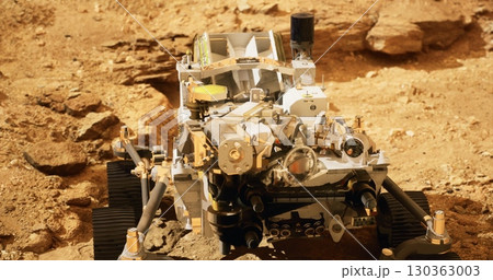 A sophisticated robotic rover traverses the rugged Martian landscape, equipped with various scientific instruments. Dust and rocky formations surround the vehicle as it examines the planets geology. 130363003