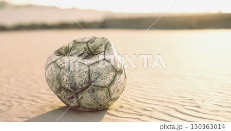 A weathered soccer ball lies abandoned on the sandy beach, illuminated by the warm colors of sunset. The sun casts a soft glow, creating a serene atmosphere around the forgotten toy. A weathered soccer ball lies abandoned on the sandy beach, illuminated by the warm colors of sunset. The sun casts a soft glow, creating a serene atmosphere around the forgotten toy. 130363014