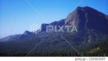 Towering peaks rise proudly against the bright blue sky, surrounded by a sea of lush green trees. The beauty of nature is highlighted in this stunning midday panorama, inviting exploration. Towering peaks rise proudly against the bright blue sky, surrounded by a sea of lush green trees. The beauty of nature is highlighted in this stunning midday panorama, inviting exploration. 130363097
