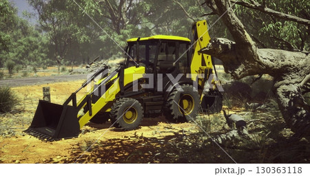 A vibrant yellow backhoe loader stands ready for action in a sunlit, rugged landscape. Surrounding trees sway gently, hinting at the days warm weather while the vehicle prepares to clear debris. 130363118