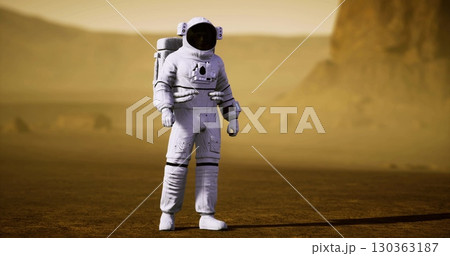 An astronaut stands on the red planets surface, surrounded by rocky terrain and dusty horizons. The Martian atmosphere creates a hazy backdrop for this extraordinary exploration. 130363187