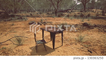 In a desolate landscape, a weathered table and chair sit forlornly on dry ground surrounded by sparse vegetation and scattered rocks under the midday sun, evoking a sense of isolation and nostalgia. In a desolate landscape, a weathered table and chair sit forlornly on dry ground surrounded by sparse vegetation and scattered rocks under the midday sun, evoking a sense of isolation and nostalgia. 130363250