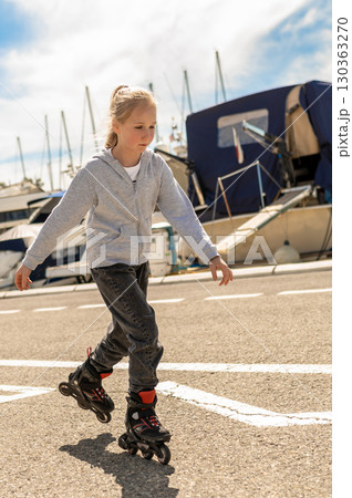 Happy child on rollerblades riding by boats at harbor spending free time Happy child on rollerblades riding by boats at harbor spending free time 130363270