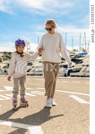 Young girl wearing rollerblades and helmet holds hands with woman near the marina Young girl wearing rollerblades and helmet holds hands with woman near the marina 130363301