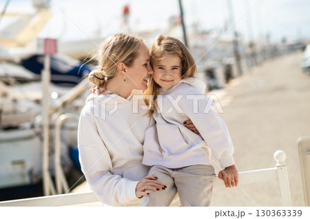 Mother hugging daughter on pier near yachts and calm blue water Mother hugging daughter on pier near yachts and calm blue water 130363339