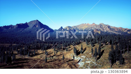 Expansive landscape features rolling hills and towering mountains bathed in sunlight. Lush evergreen trees blanket the ground, creating a tranquil haven in natures embrace. Expansive landscape features rolling hills and towering mountains bathed in sunlight. Lush evergreen trees blanket the ground, creating a tranquil haven in natures embrace. 130363894