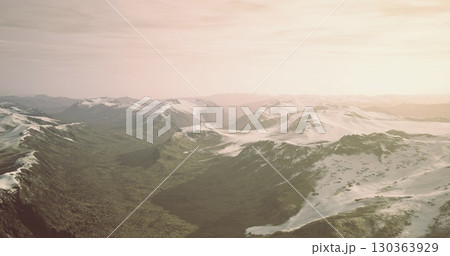 Waves of majestic mountains stretch endlessly, their snow capped summits glowing in the soft light of dawn. Valleys below cradle lush green terrain, showcasing natures serene beauty. 130363929