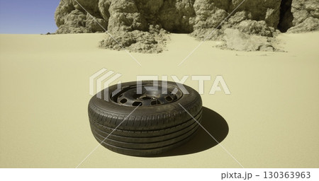 A worn tire is positioned on sandy terrain surrounded by rugged rock formations under a clear blue sky. The rugged environment creates a striking contrast with the tire. 130363963