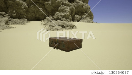A vintage suitcase rests on the barren sandy landscape, with rugged rock formations towering in the background under a clear blue sky. The setting appears desolate yet intriguing. 130364057