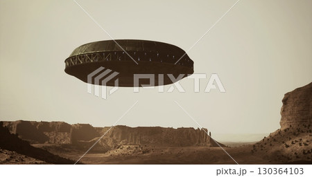 A UFO hovers above a rocky landscape characterized by rugged cliffs and barren ground during twilight. The object displays a circular shape with glowing lights along its perimeter. A UFO hovers above a rocky landscape characterized by rugged cliffs and barren ground during twilight. The object displays a circular shape with glowing lights along its perimeter. 130364103