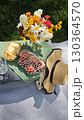 Colorful summer picnic setup with fresh flowers, peaches in a mesh bag, crackers and a straw hat on a blanket 130364570