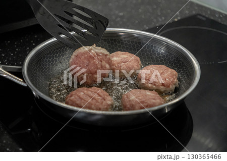Raw cutlets sizzle in a hot frying pan on a modern stovetop, being flipped by a spatula during home cooking for a delicious meal preparation Raw cutlets sizzle in a hot frying pan on a modern stovetop, being flipped by a spatula during home cooking for a delicious meal preparation 130365466