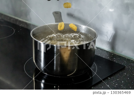 Delicious pasta falling into a shiny stainless steel pot of boiling water on a modern induction hob, symbolizing home meal preparation Delicious pasta falling into a shiny stainless steel pot of boiling water on a modern induction hob, symbolizing home meal preparation 130365469