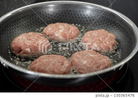 Five uncooked meat cutlets sizzling and bubbling in hot oil within a textured frying pan, demonstrating active cooking for a delicious homemade meal preparation Five uncooked meat cutlets sizzling and bubbling in hot oil within a textured frying pan, demonstrating active cooking for a delicious homemade meal preparation 130365476