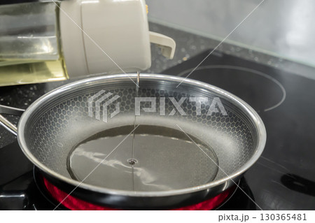 Cooking oil is poured into a hot frying pan on a modern induction hob, symbolizing healthy meal preparation in a contemporary kitchen 130365481