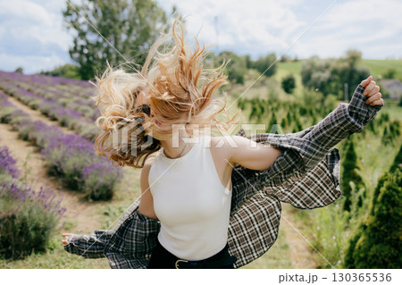 Happy young blonde woman wearing casual clothes is spinning around with open arms and hair flying in the air, enjoying freedom in a beautiful lavender field in a sunny summer day. Carefree spirit Happy young blonde woman wearing casual clothes is spinning around with open arms and hair flying in the air, enjoying freedom in a beautiful lavender field in a sunny summer day. Carefree spirit 130365536