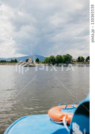 Pedal boat gliding across tranquil lake, surrounded by sailboat and cloudy sky, creating peaceful scene of leisure and recreation in natura embrace. Pedal boat gliding across serene lake waters Pedal boat gliding across tranquil lake, surrounded by sailboat and cloudy sky, creating peaceful scene of leisure and recreation in natura embrace. Pedal boat gliding across serene lake waters 130365539